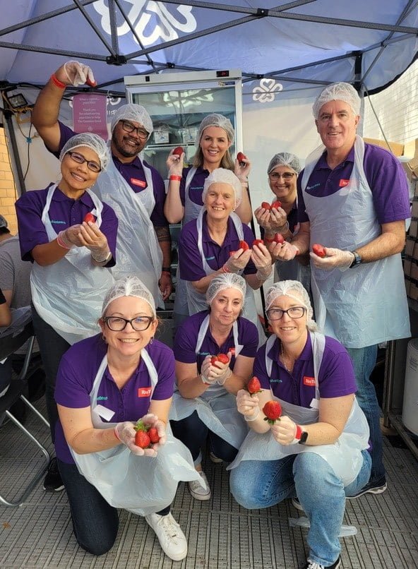 Rio Tinto volunteer team holding up Queensland strawberries behind the Ekka Strawberry Sundae Stalls